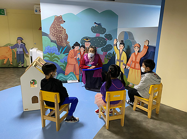 할머니가 3명의 아이들에게 전시장에 앉아 이야기를 들려주는 모습